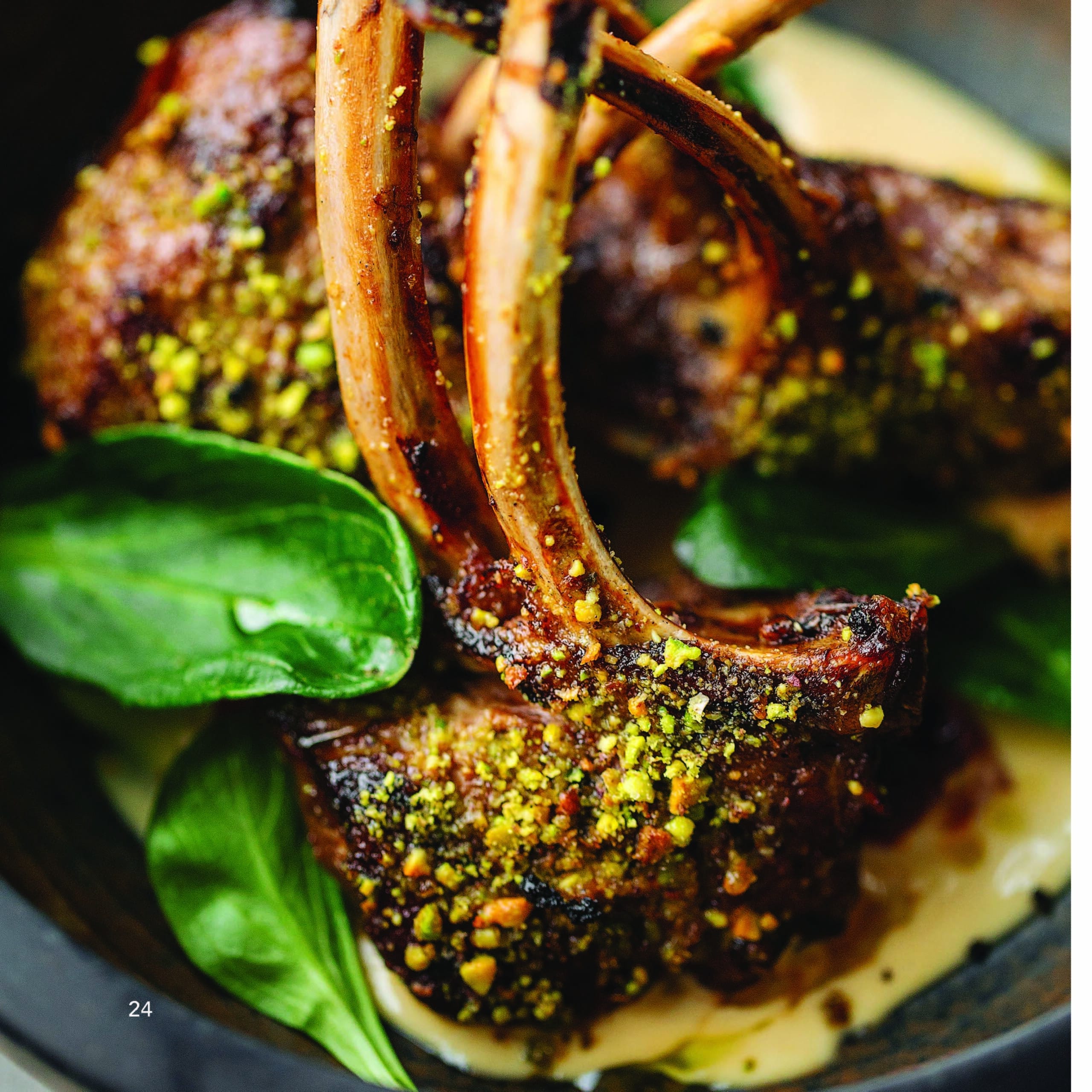 Close-up of herb-crusted lamb chops served with a creamy sauce and garnished with fresh spinach leaves.