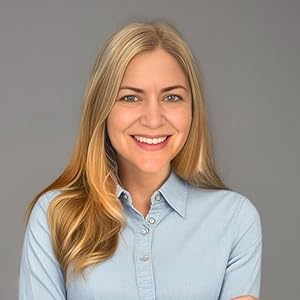 A smiling woman with long blonde hair wearing a blue button-up shirt, standing with her arms crossed against a gray background.
